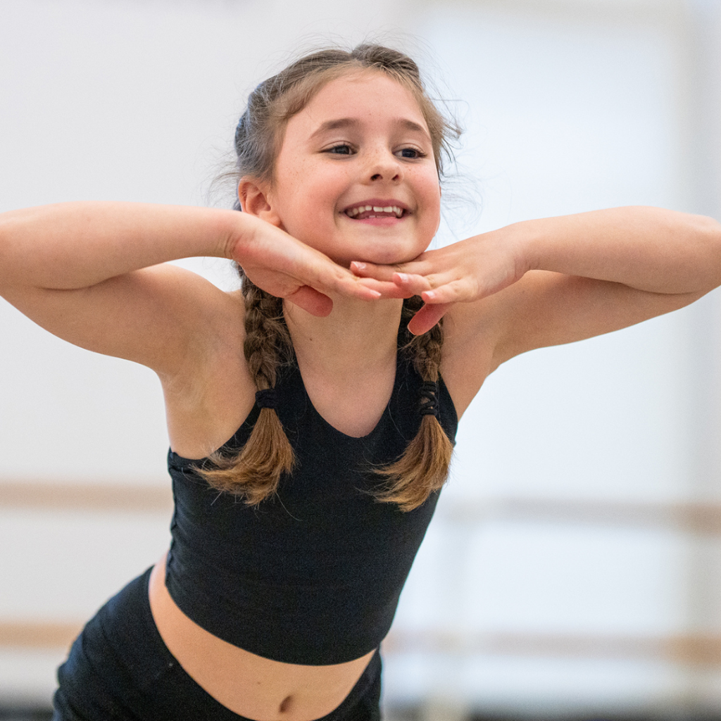 young female dancer in Steps studios - leaning forward with hands under her chin, elbows out and a big smile