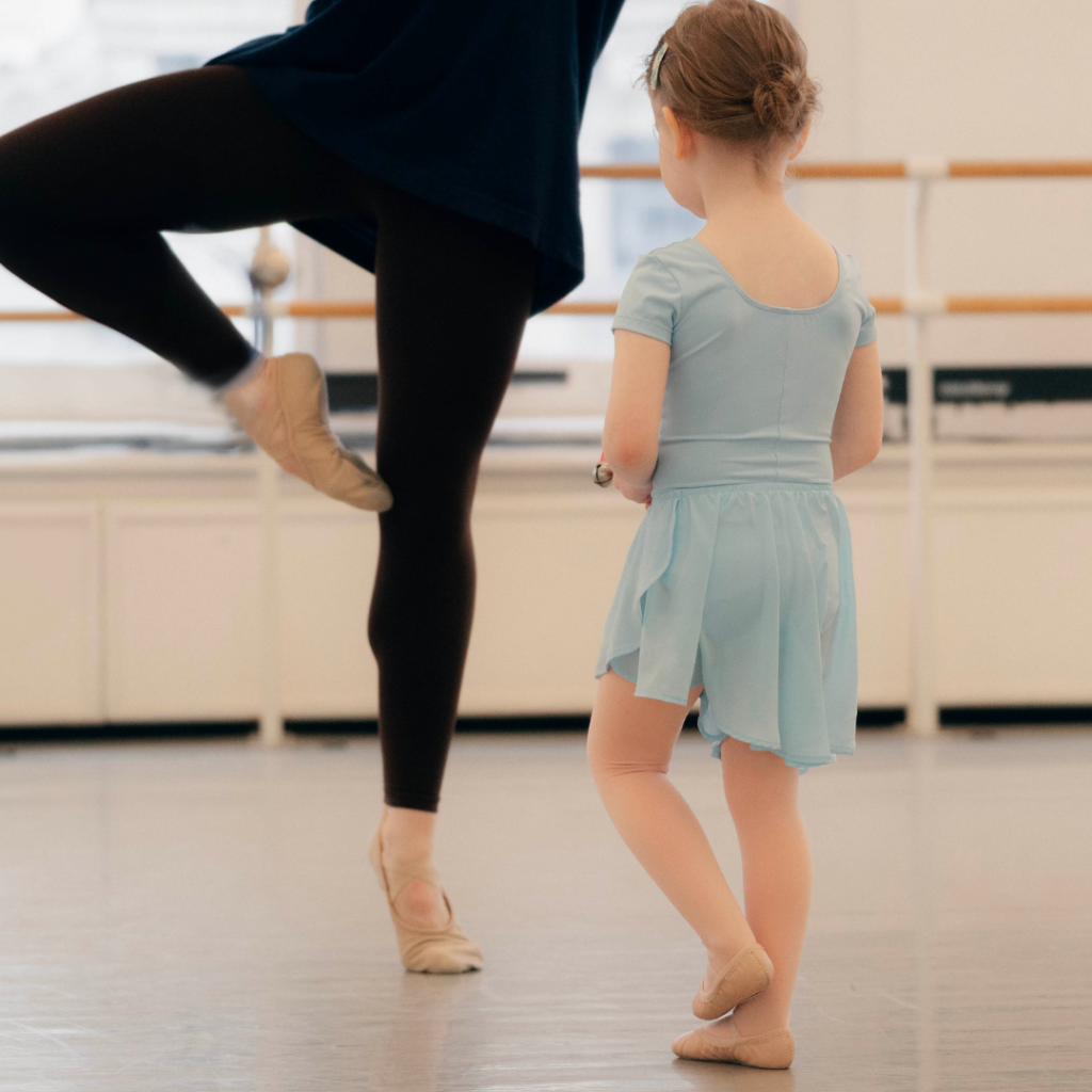 Steps first steps dancer in blue leotard and dance skirt standing before a ballet dancer in black tights and dance skirt in Retiré