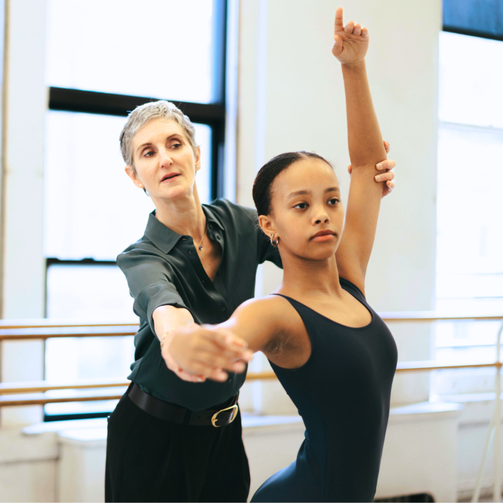 Jen Kreichman, director of the Steps on Broadway Academy is assisting an academy dancer in Steps dance studios - New York City visible through the windows above the barre
