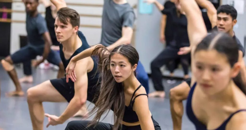 A group of dance students in a modern dance class at Steps on Broadway - crouching, with arms spread down and back