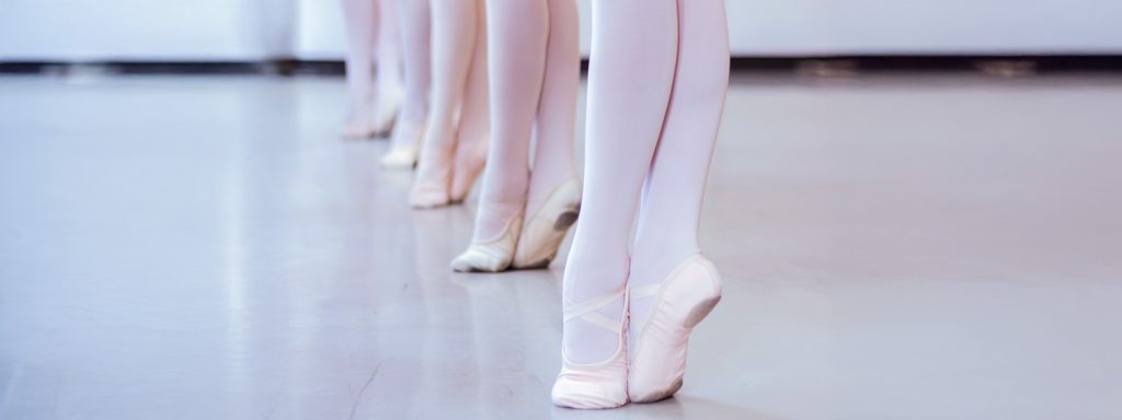 photo of the feet of five ballet dancers in pink ballet slippers on their toes