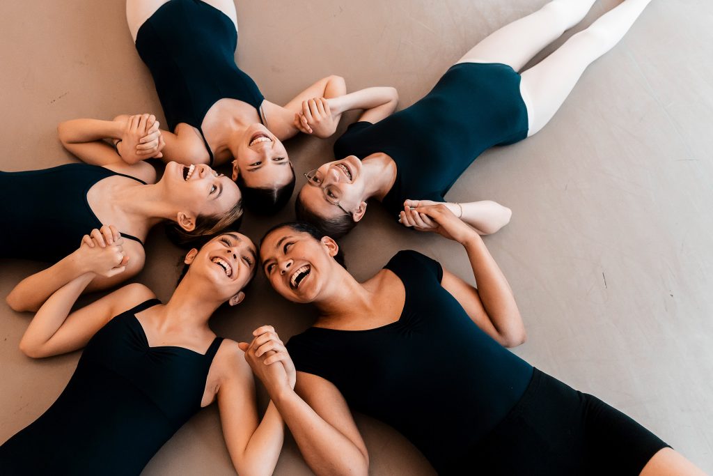 Photo of smiling Steps on Broadway Academy dancers lying on their backs, heads all together and holding hands in a starfish shape