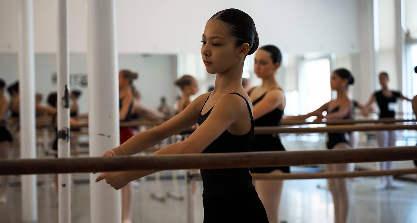 Six ballet dancers at the barre with steps logo above