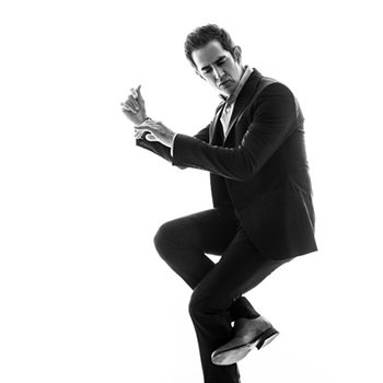black and white photo of Andy Blankenbuehler dancing in dark suit on white background