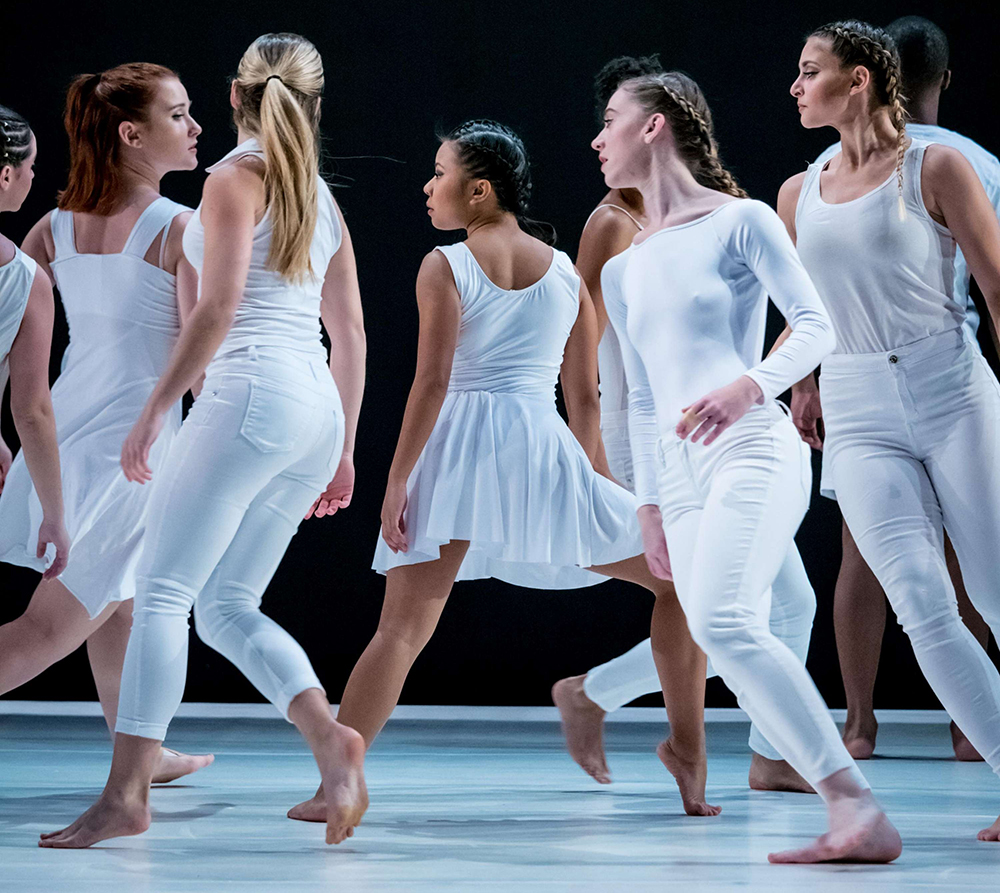 Montclair State University Dancers all in white moving quickly on stage