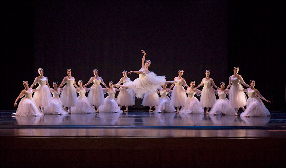 Large group of University of Missouri - Kansas City ballet dancers on stage - one in front leaping