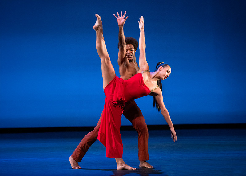 Two Juilliard Dance students performing in red on a stage lit with blue light