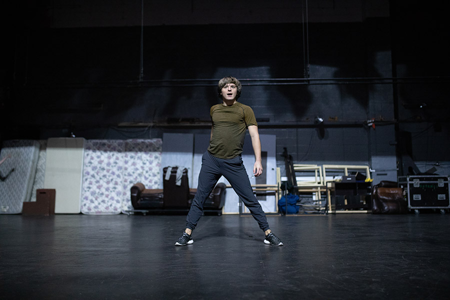 One man in a green shirt and blue pants posed fiercely on stage in a tech rehearsal